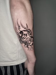 Oni mask tattoo in Neo Japanese style with fire and bold blackwork lines, representing anger, protection, and inner strength.